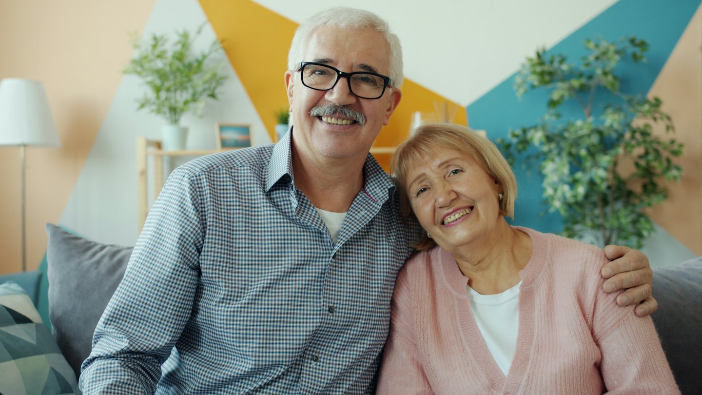 Smiling older couple posing arm-in-arm on a sofa.